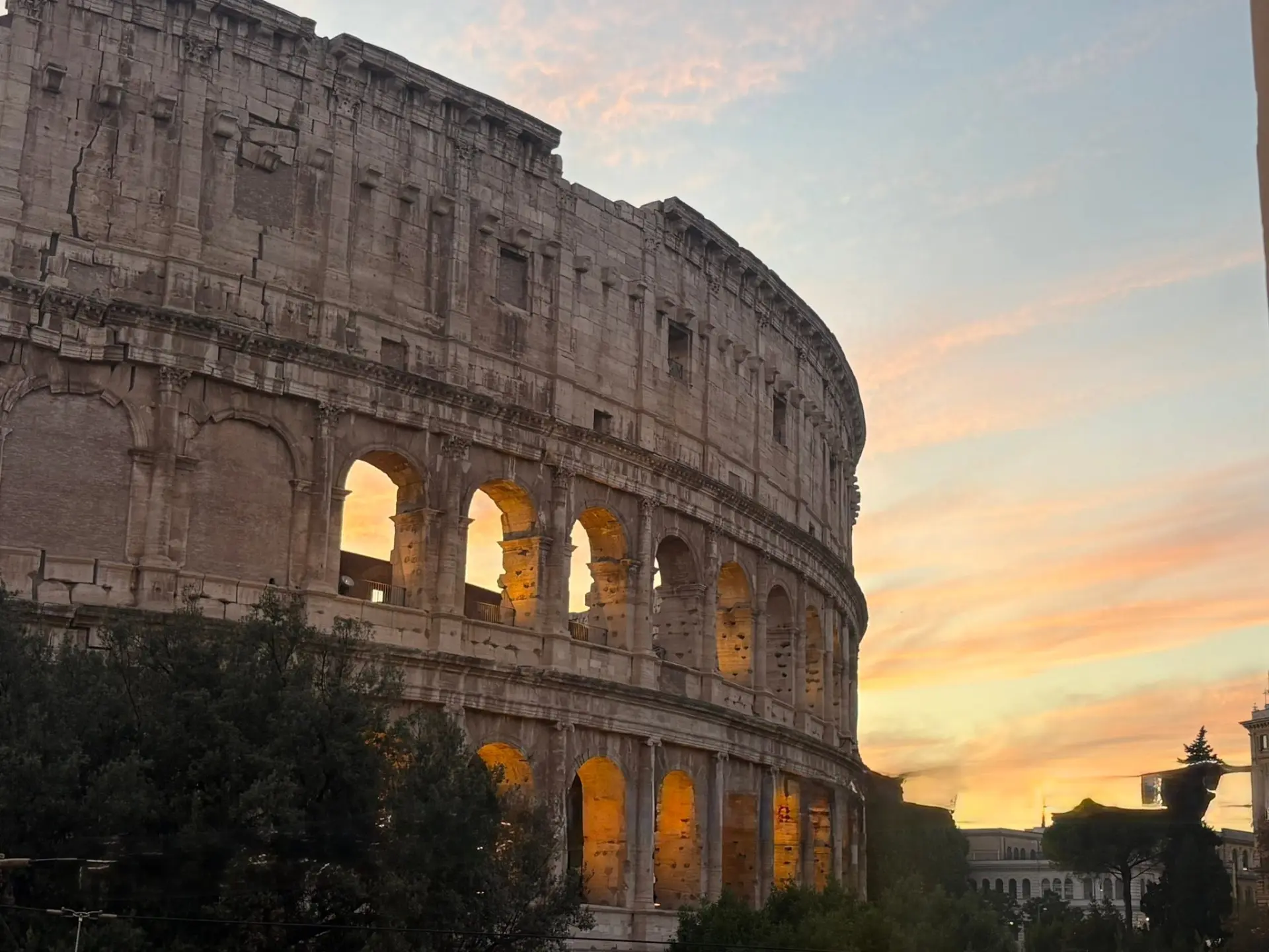 The Colosseum in Rome glowing at sunset, golden light shining through its arches under a pink sky